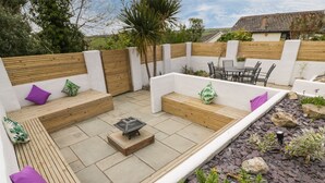 A patio with a fire pit, wooden benches, and a table with chairs. - Estuary View (Newquay)