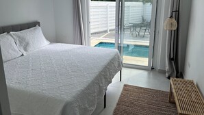 A bedroom with a bed, a view of a swimming pool, and a sliding glass door to the outside.