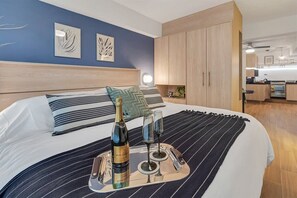 Et moderne hotelværelse med en seng, et natbord med en flaske og glas, samt udsigt til køkkenet.