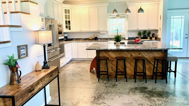 Cocina moderna con armarios blancos, una isla grande con taburetes, electrodomésticos de acero inoxidable e iluminación colgante.