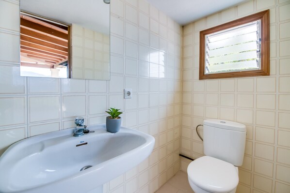 Un baño con un lavamanos blanco, un inodoro, una ventana con persianas y un espejo.