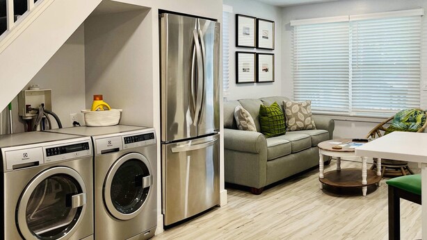 Une cuisine moderne équipée d’appareils électroménagers en acier inoxydable, d’un lave-linge et d’un sèche-linge intégrés, d’un escalier et d’un espace de vie comprenant un canapé et une table à manger.