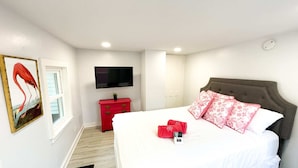 Une chambre à coucher avec un lit, une commode rouge, un téléviseur à écran plat et un tableau accroché au mur.