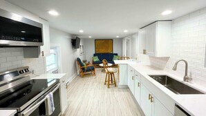 Una cocina moderna con armarios blancos, electrodomésticos de acero inoxidable y un comedor con sofá azul y sillas de madera.