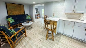 Un espacio de estar moderno con sofá, sillas, una mesa de comedor y una cocina con armarios blancos y salpicadero de azulejos.