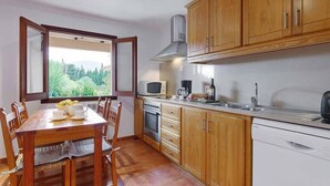 A kitchen with wooden cabinets, a dining table with chairs, a window with a view of greenery, a microwave, a coffee maker, and a dishwasher.