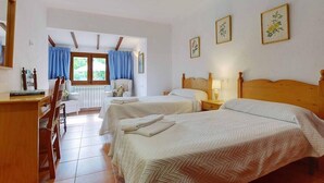 A hotel room with two beds, a desk, and a chair. There are curtains on the windows, and the room has a tiled floor.