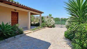 A stone-paved entrance to a building with a tiled roof, surrounded by greenery and a clear sky.