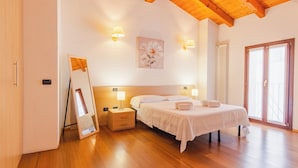 A bedroom with a wooden ceiling, a bed with white linens, two bedside lamps, a framed picture on the wall, and a window with curtains.