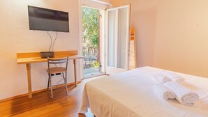 A hotel room with a bed, a desk with a chair, a television mounted on the wall, and a sliding glass door leading to an outdoor area.