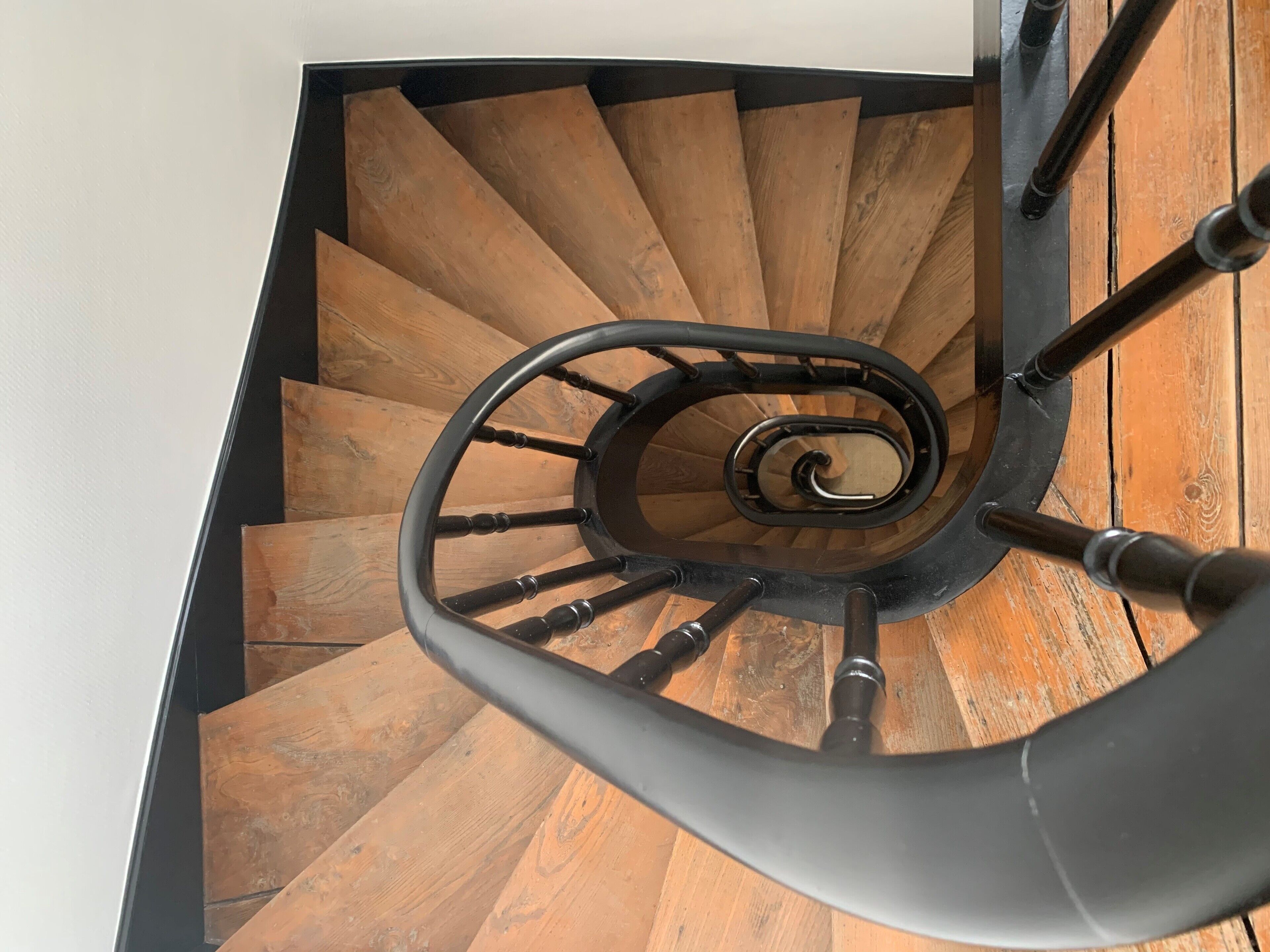 A wooden spiral staircase with black handrails and a black wall at the top.