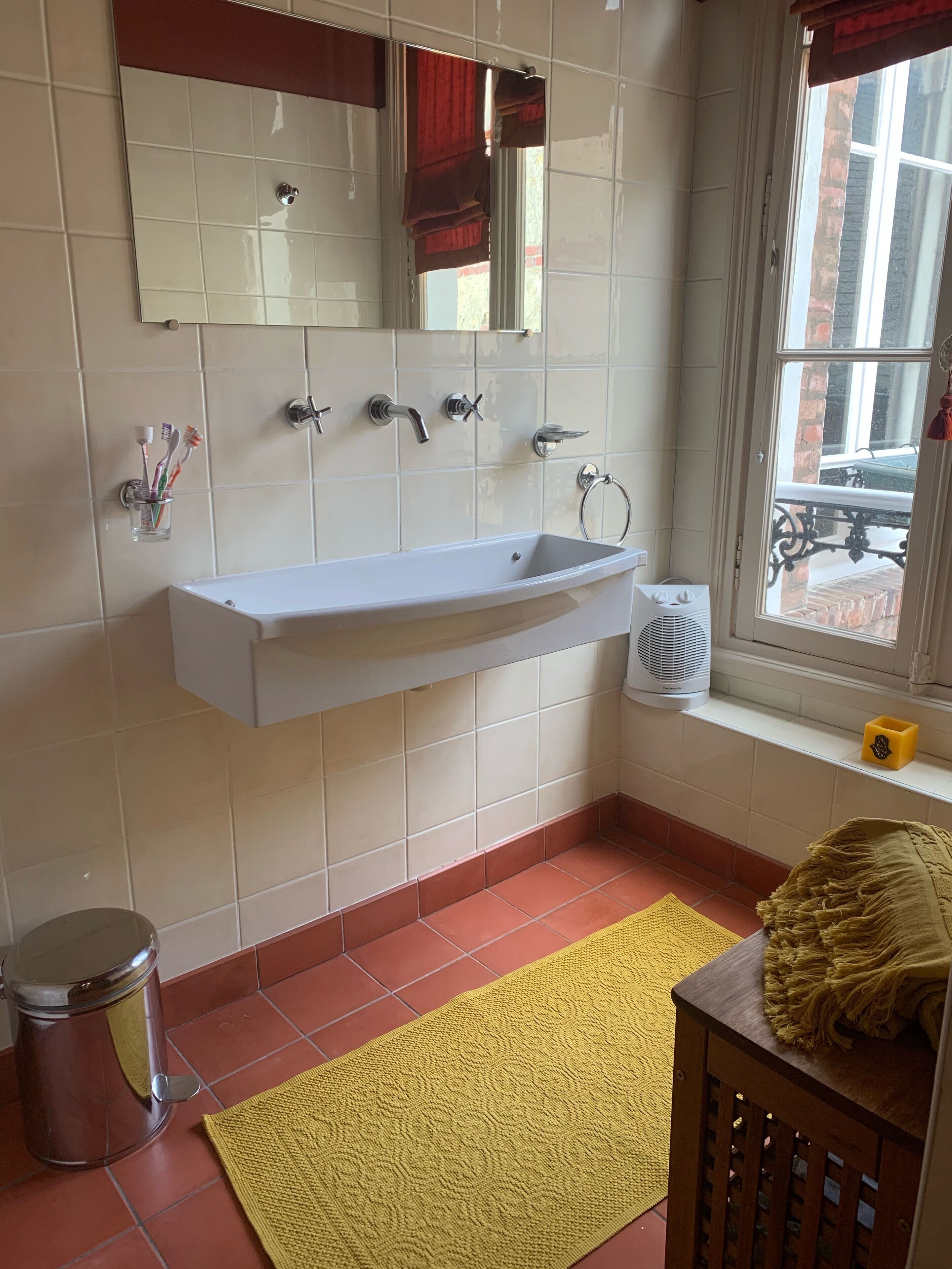 Un baño con lavamanos blanco, varios grifos, un espejo y una ventana con vistas al exterior.
