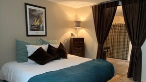 Une chambre à coucher avec un lit, des oreillers, une commode, une lampe et un tableau encadré au mur.