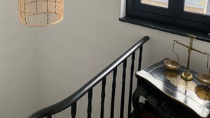 Un escalier avec une rampe noire, une fenêtre ornée d’un motif en forme de cœur et trois suspensions lumineuses en osier.