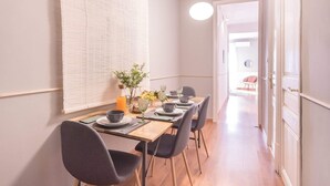A dining area with a long table set for four, chairs, a vase with flowers, and a bottle of orange juice. - Sweett | Rocafort 102 (Barcelona)