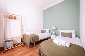 A hotel room with two beds, a wooden drying rack, a nightstand with toiletries, and a green wall. - Sweett | Rocafort 203 (Barcelona)