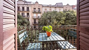 A balcony with a table and chairs, a potted plant, and a view of multi-story buildings. - Sweett | Rocafort 203 (Barcelona)