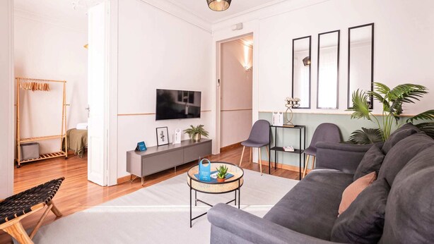 A modern living room with a grey sofa, a TV, a small side table, and a plant. - Sweett | Rocafort 203 (Barcelona)