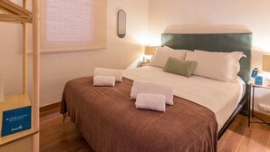 Une chambre d’hôtel avec un lit, une table de chevet, une lampe et une fenêtre avec des stores.