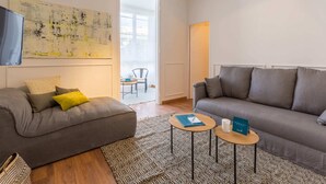 Un salon moderne avec un canapé gris, un tapis à motifs et une petite table ronde sur laquelle sont posés un livre et une bougie.