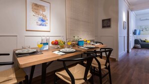 Un coin repas avec une table en bois dressée pour quatre personnes, des chaises et un buffet garni de fruits et de boissons.