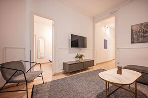 A modern living room with a sofa, a chair, a small table, a TV mounted on the wall, and a painting. - Sweett | Rocafort Principal 3 (Barcelona)