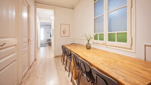 A long dining table with chairs, a vase with flowers, and a window with green and blue panes. - Sweett | Rocafort Principal 3 (Barcelona)