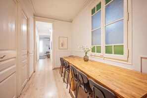 A long dining table with chairs, a vase with flowers, and a window with green and blue panes. - Sweett | Rocafort Principal 3 (Barcelona)