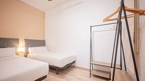 A hotel room with two beds, a bedside table with a lamp, a wooden wardrobe, and a window with a curtain. - Sweett | Rocafort Principal 3 (Barcelona)