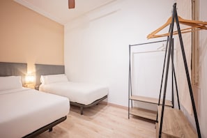 A hotel room with two beds, a bedside table with a lamp, a wooden wardrobe, and a window with a curtain. - Sweett | Rocafort Principal 3 (Barcelona)