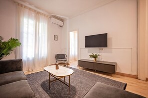 A modern living room with a sofa, a coffee table, a TV mounted on the wall, and a potted plant. - Sweett | Rocafort Principal 3 (Barcelona)