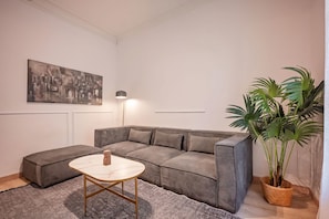 A modern living room with a sectional sofa, a small round table, a floor lamp, and a large potted plant.
