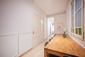A room with a wooden dining table, chairs, a vase with flowers, and a window with a view.