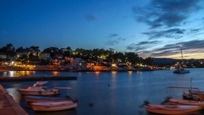 Une ville côtière au crépuscule, avec des bateaux amarrés le long du port, des bâtiments illuminés et une mer calme.