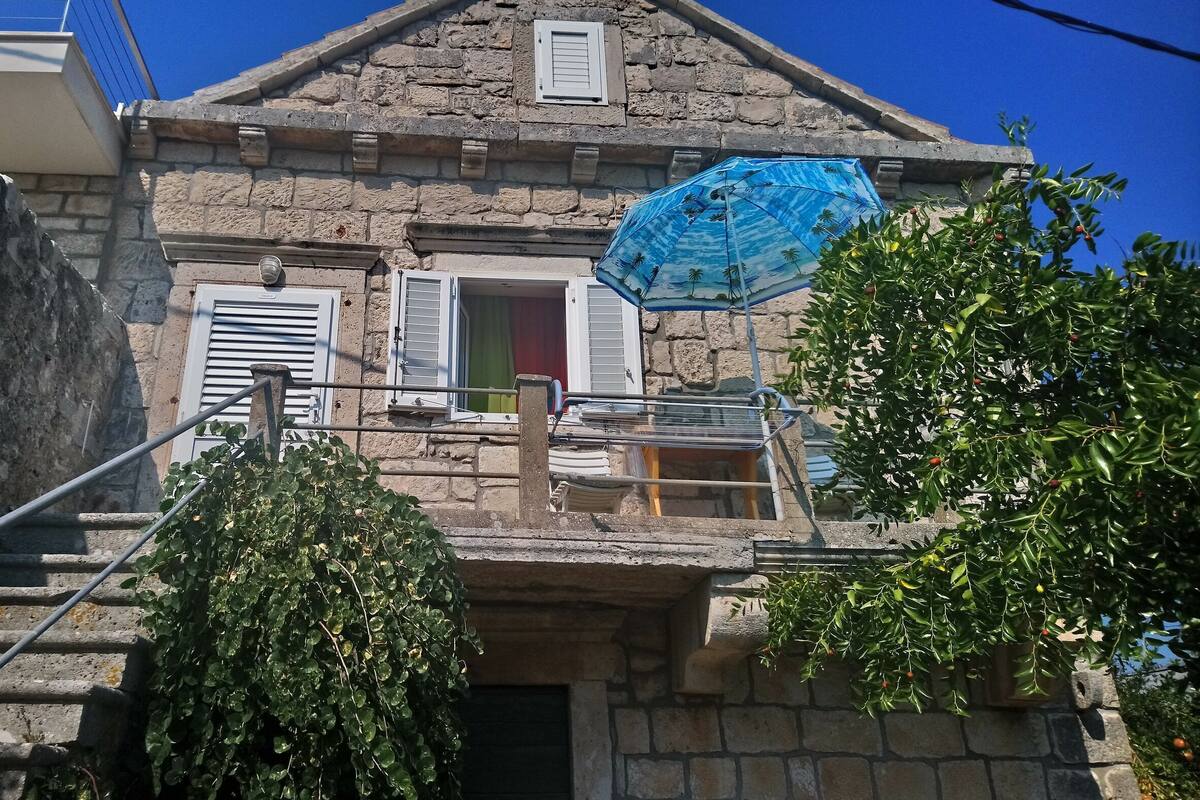 A stone building with a balcony, a staircase, and a blue umbrella.