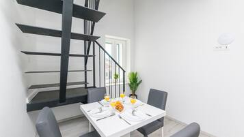 A dining area with a white table set for four, a black staircase, and a potted plant.