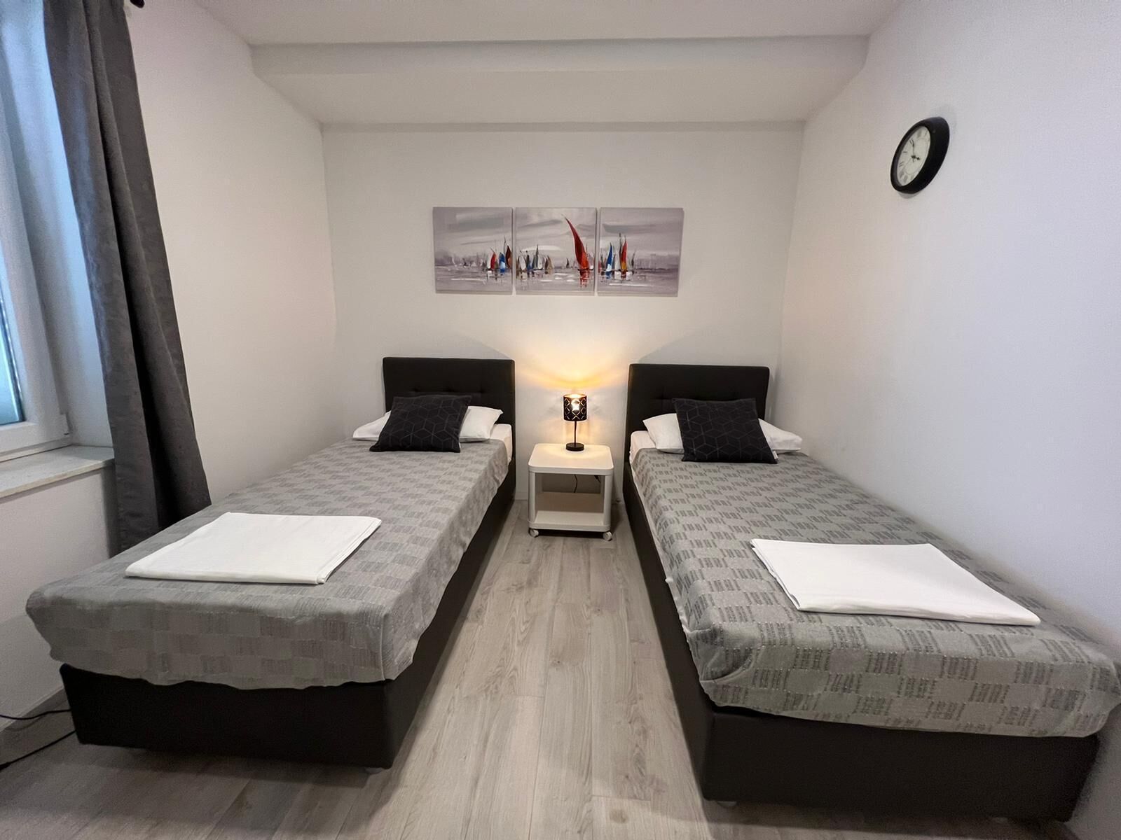 A twin room with two beds, a nightstand, a lamp, and a painting on the wall.