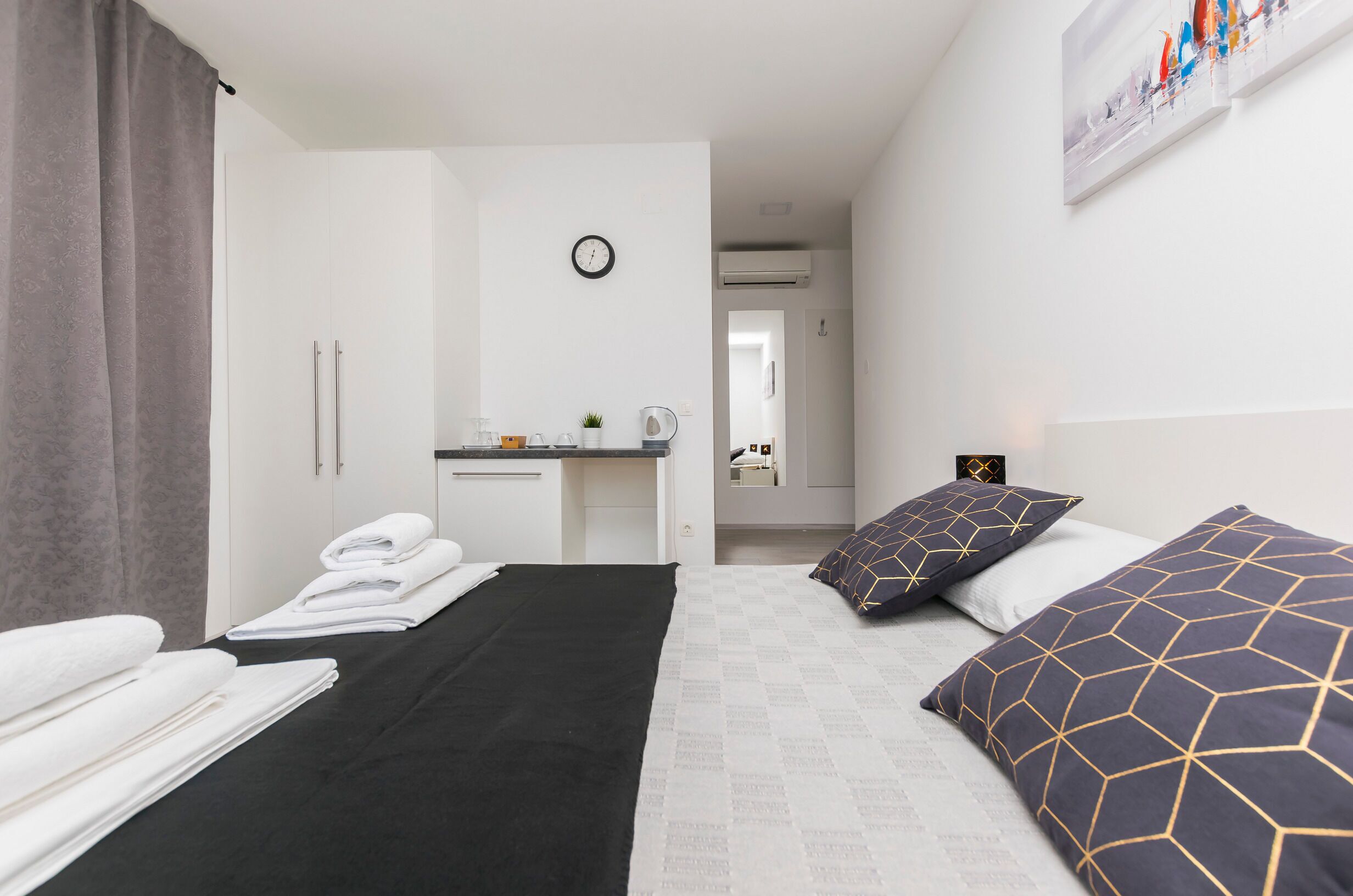Ein Hotelzimmer mit Bett, Schreibtisch und Spiegel. Auf dem Bett liegen Handtücher und an der Wand hängt eine Uhr.