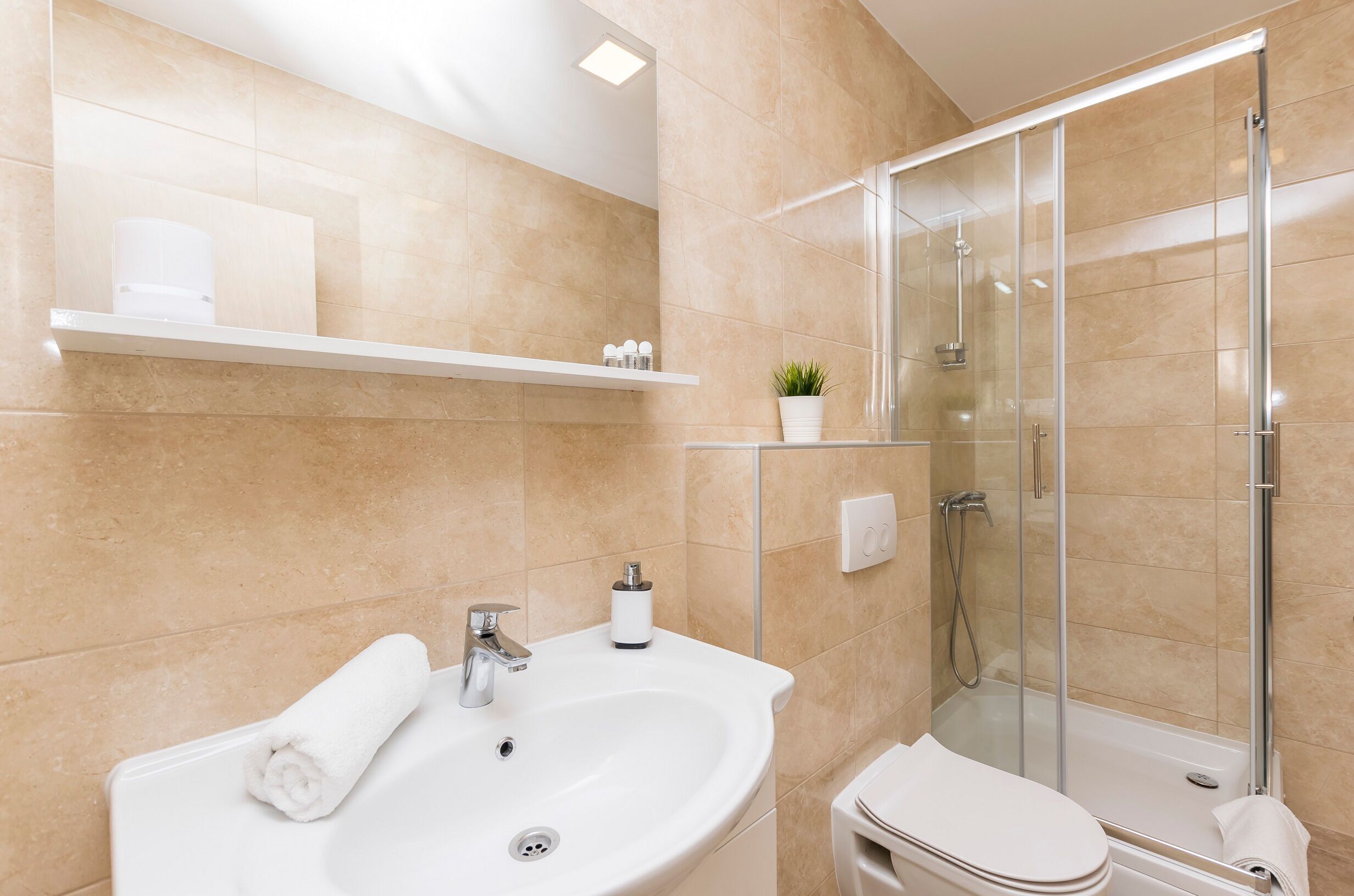 A modern bathroom with a white sink, a glass shower enclosure, and beige tiles.