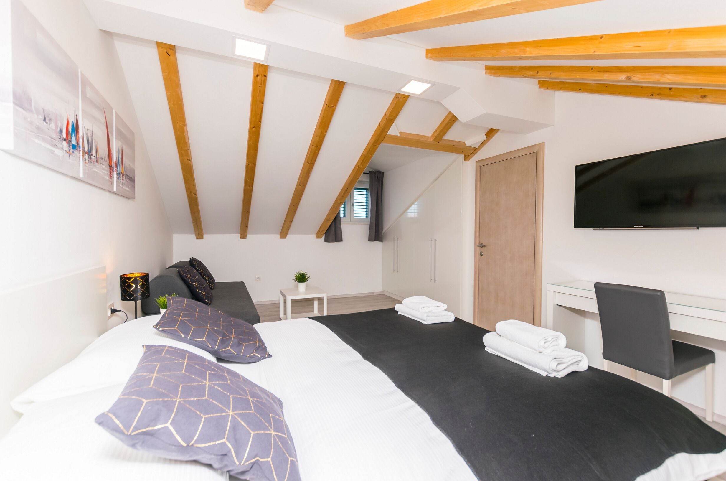 Ein modernes Schlafzimmer mit einem großen Bett, einem Flachbildfernseher und einem Schreibtisch mit Stuhl.