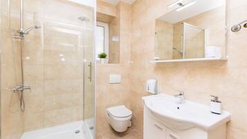 Un baño moderno con ducha envuelta en vidrio, inodoro y lavamanos con espejo arriba.