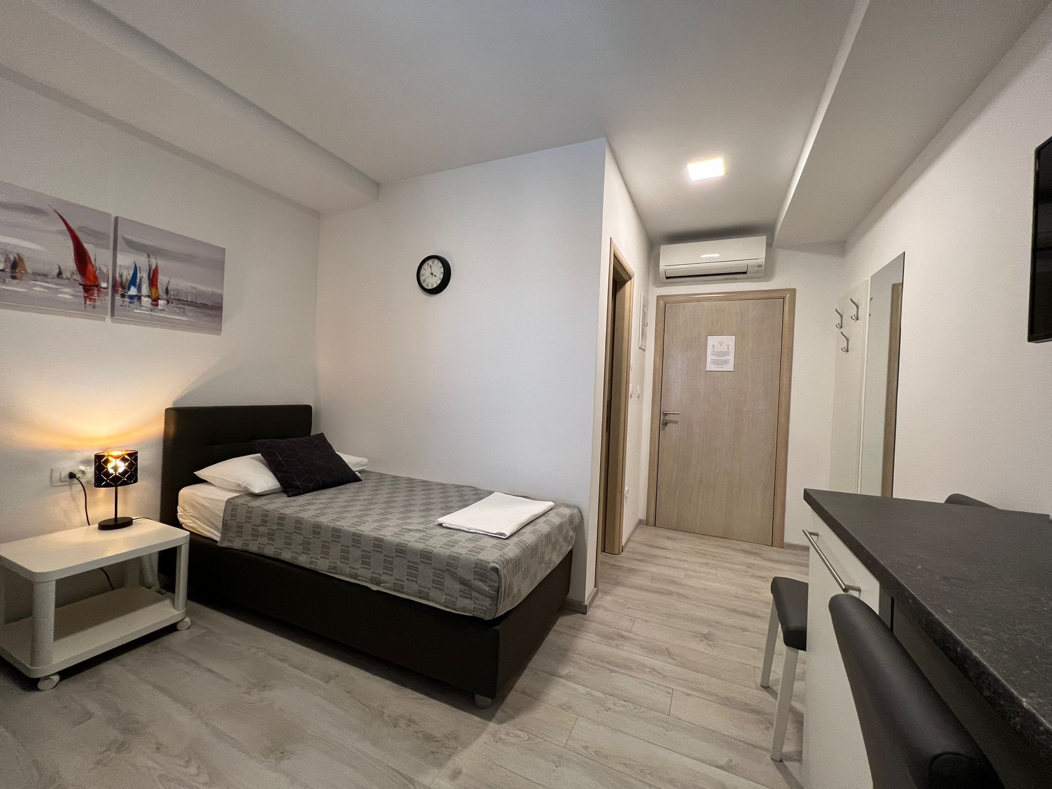 A bedroom with a bed, bedside table, lamp, and a small desk area.