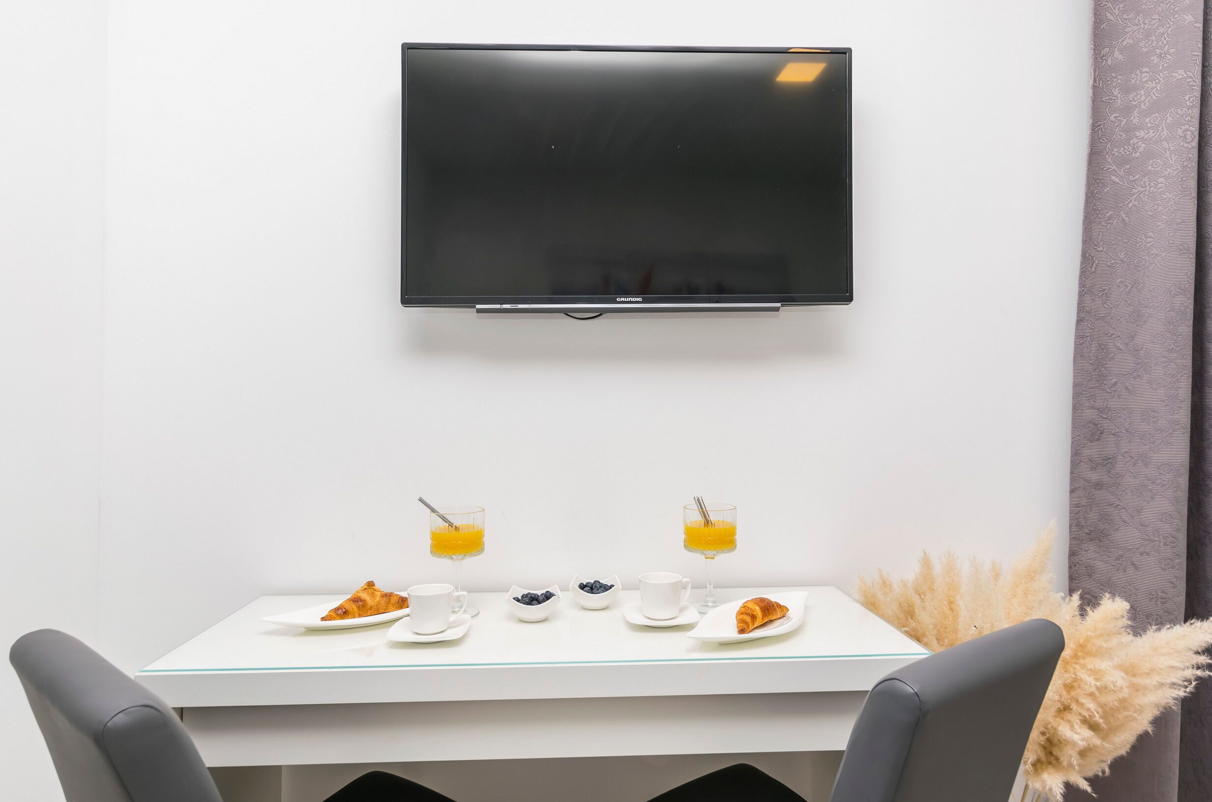 Een moderne eetruimte met een flatscreen televisie aan de muur, een witte tafel met twee stoelen en een glazen scheidingswand.