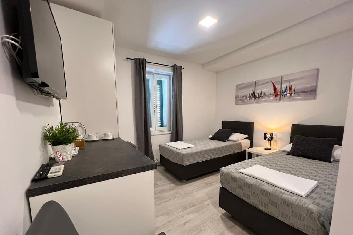 Une chambre d’hôtel moderne équipée de deux lits, d’un bureau, d’une télévision et d’une fenêtre avec des rideaux.
