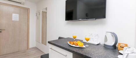 A modern kitchen with a flat-screen TV, a breakfast setup with croissants and orange juice, and a kettle.