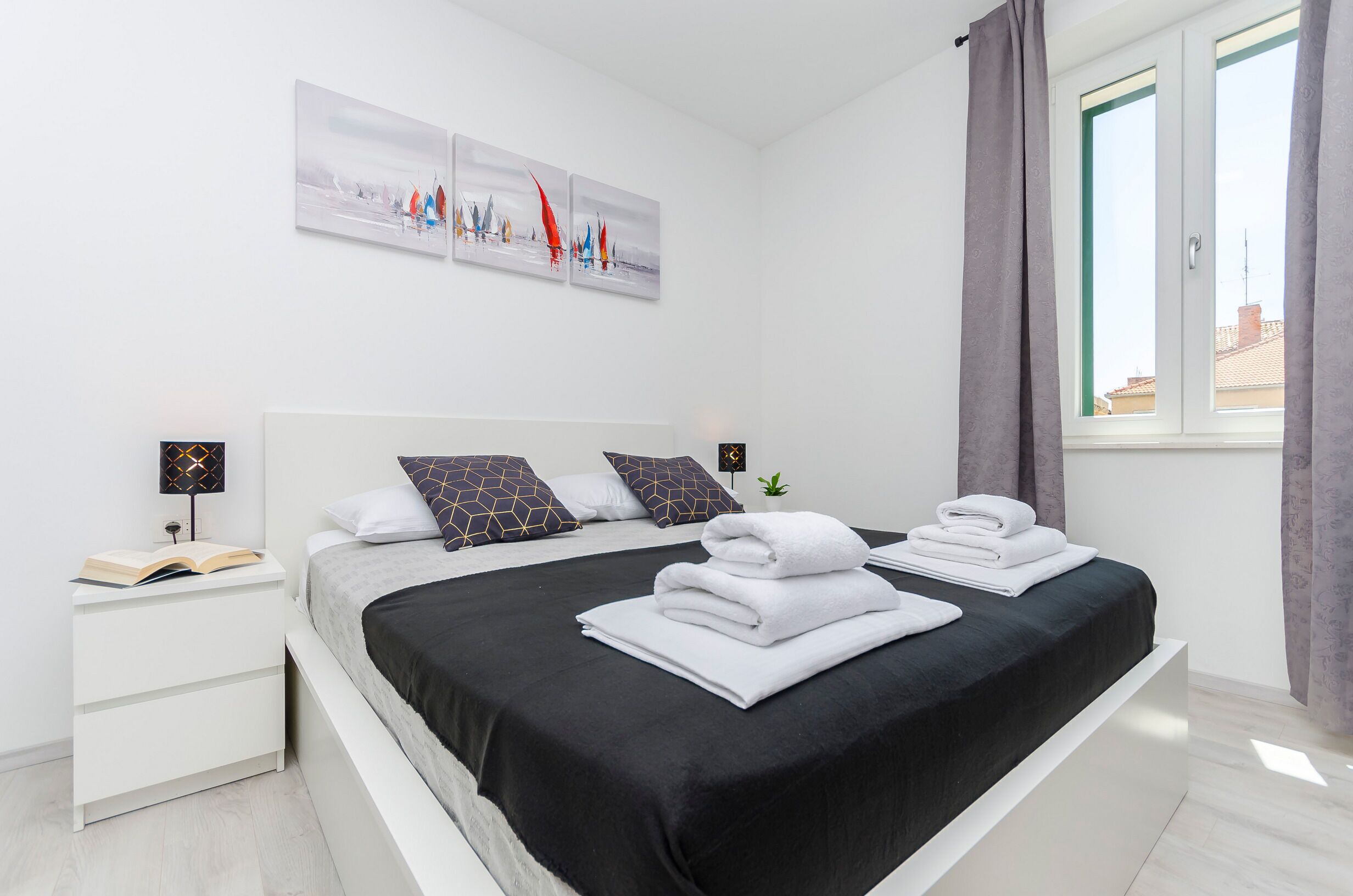 Ein modernes Schlafzimmer mit einem Bett, einem Nachttisch, einem Fenster mit Vorhängen und einem Kunstwerk an der Wand.