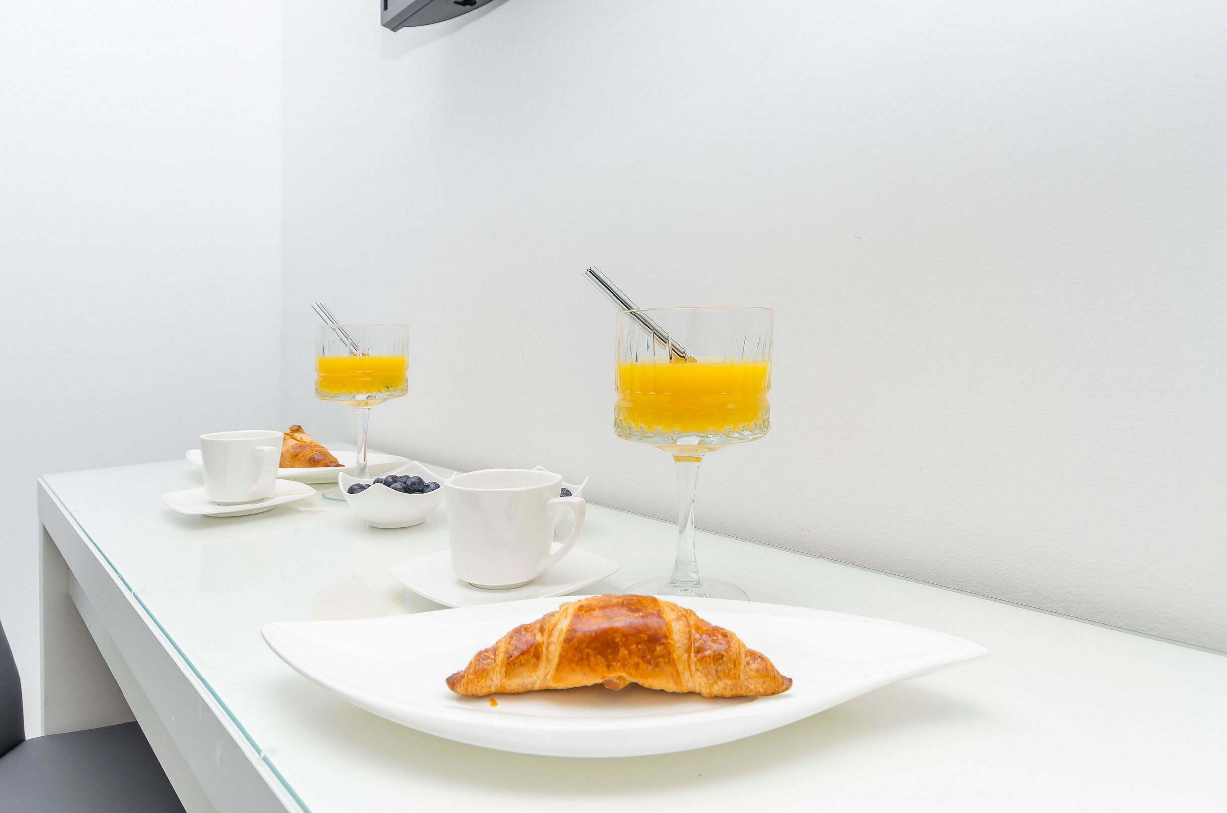 Desayuno con cruasanes, café y jugo de naranja sobre una mesa blanca.