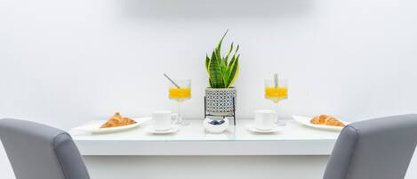 Un comedor moderno con una televisión de pantalla plana sobre una mesa blanca, dos sillas y una planta en maceta.