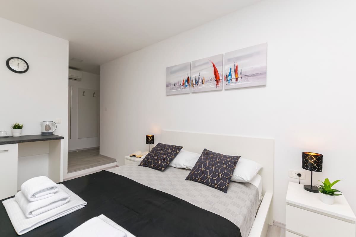 Une chambre d’hôtel moderne, équipée d’un lit, d’une table de chevet avec une lampe, d’une petite table avec un téléphone, d’une horloge murale et d’un tableau au-dessus du lit.