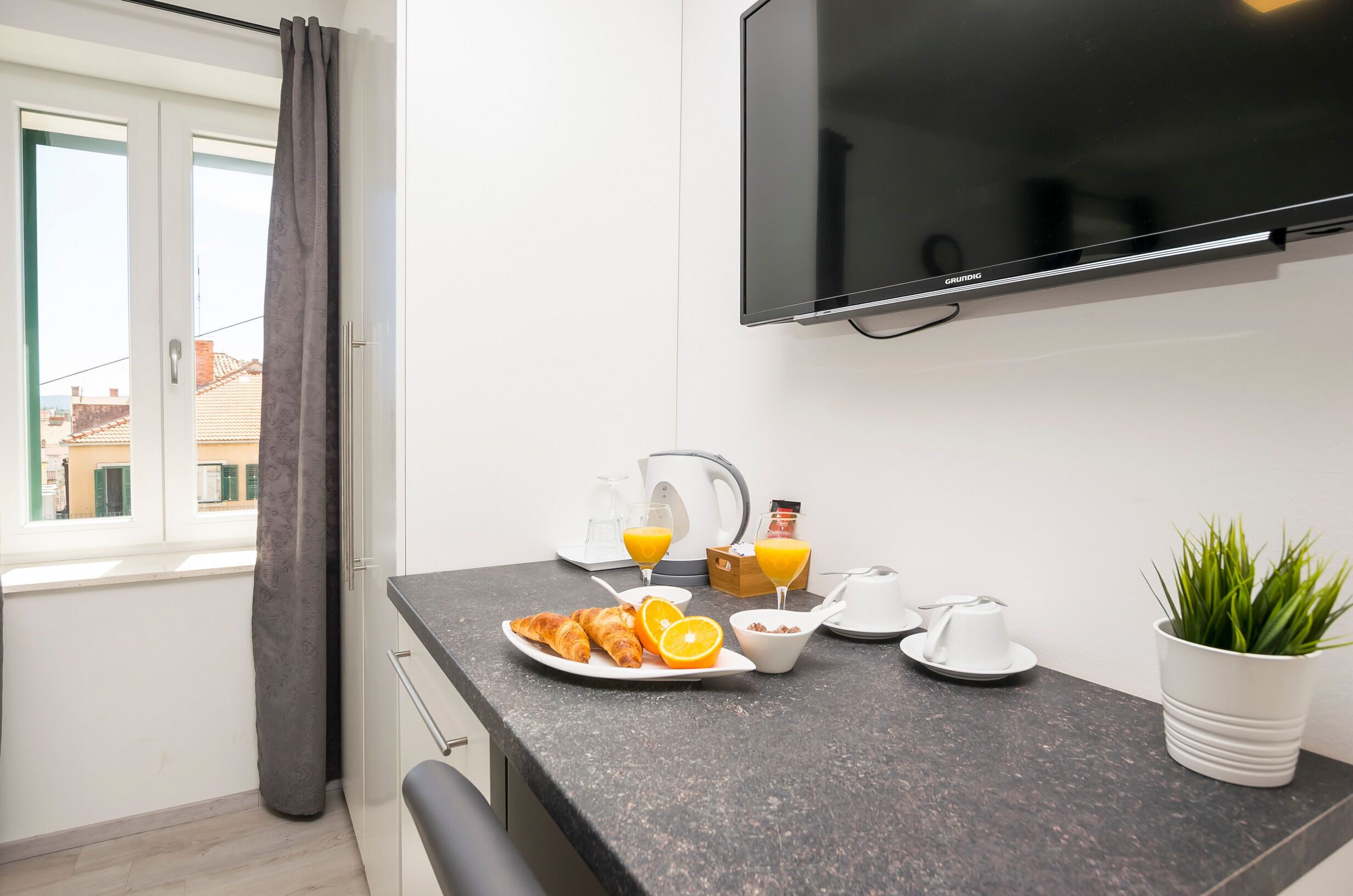 A modern kitchen with a flat-screen TV, breakfast items, and a potted plant.